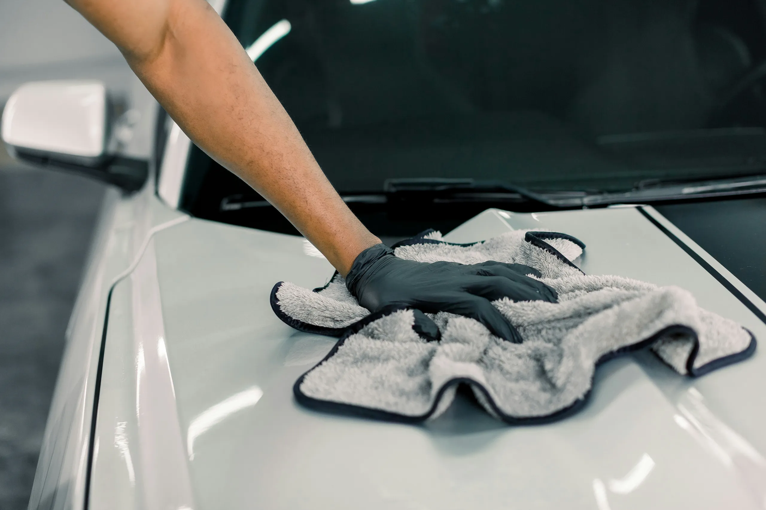 Una mano con guante limpia la pintura del coche con una microfibra